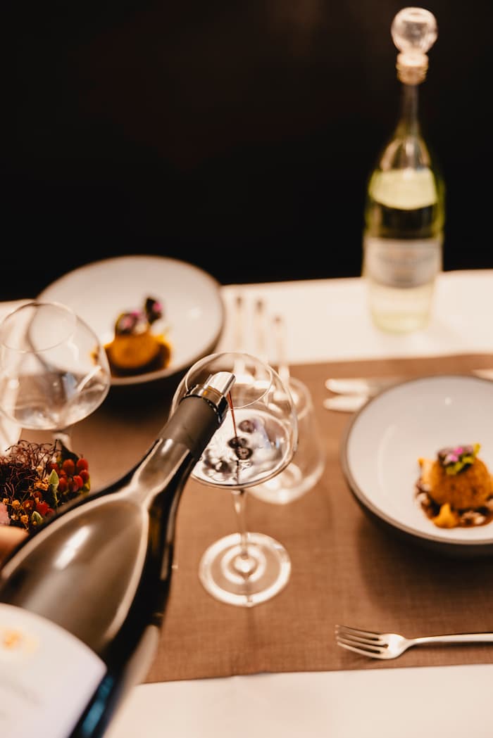 Vertikale Komposition mit raffiniertem Tischgedeck, Weinservice und Gourmet-Präsentation im eleganten Speisesaal des Restaurants.