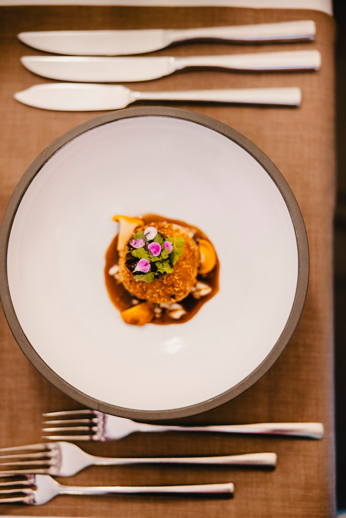 Hochformataufnahme kulinarischer Kunst: sorgfältig angerichtetes Gericht mit künstlerischen Garnituren und professioneller Präsentation auf dunklem Geschirr.